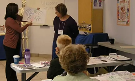 room setup like a class room with 2 women lecturing and holding up a graph